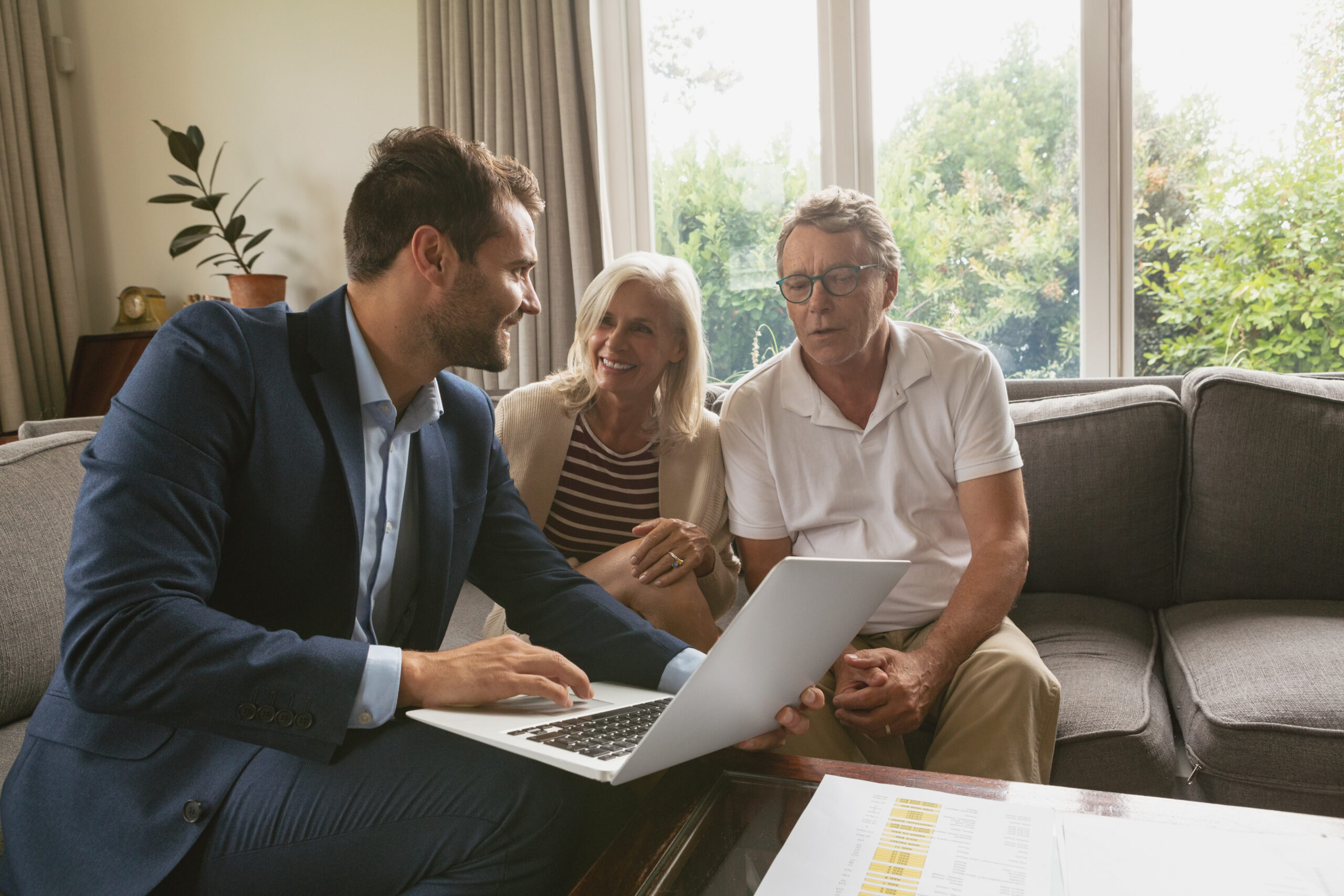 Front view of active senior Caucasian couple discussing with real estate agent over laptop in living room at home