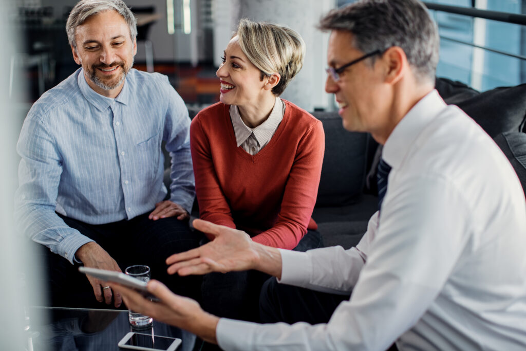 Happy mid adult couple and their financial advisor reading plans on touchpad during a meeting in the office.