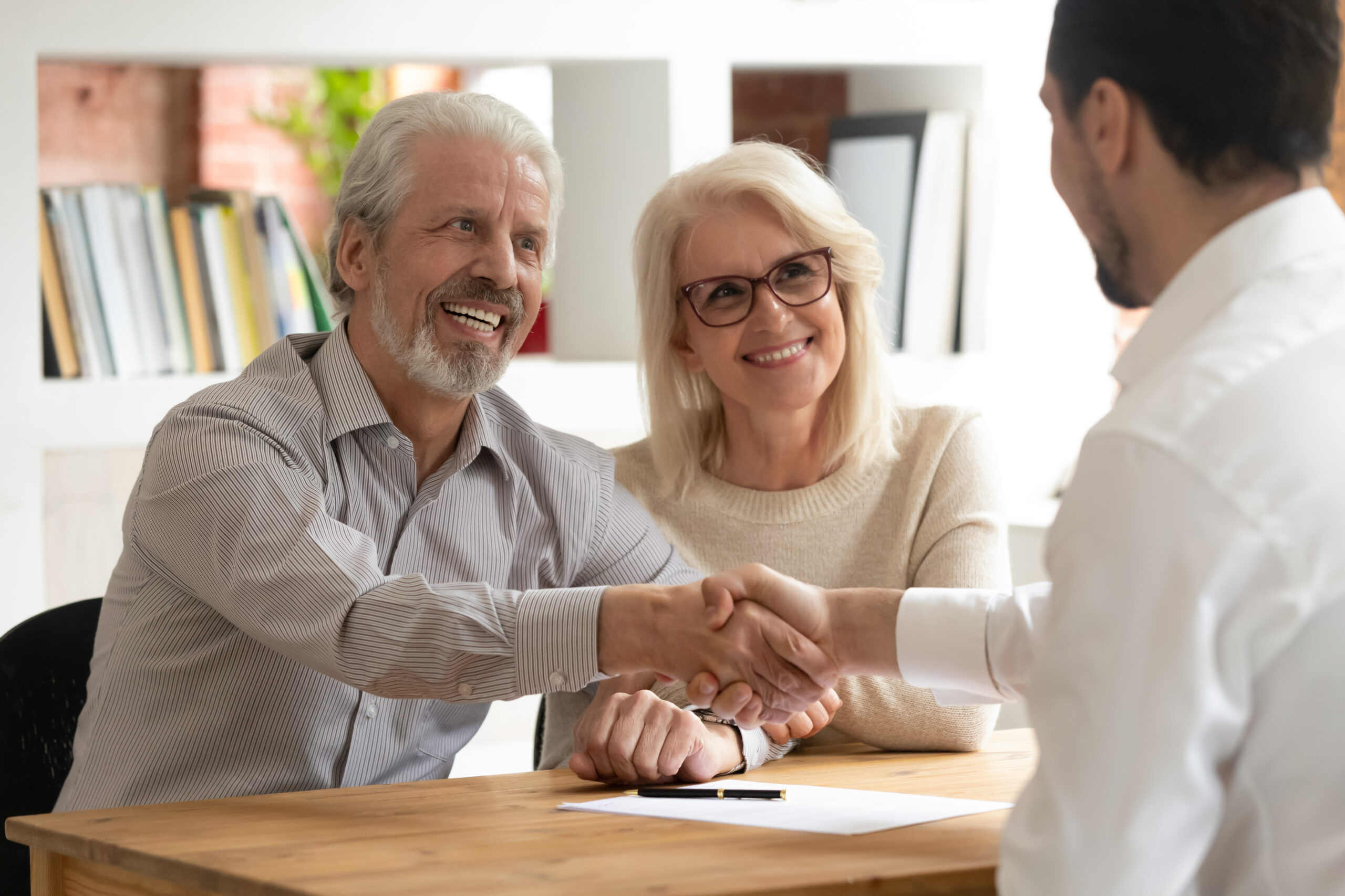 Older couple smiling and shaking hands with a professional in office.