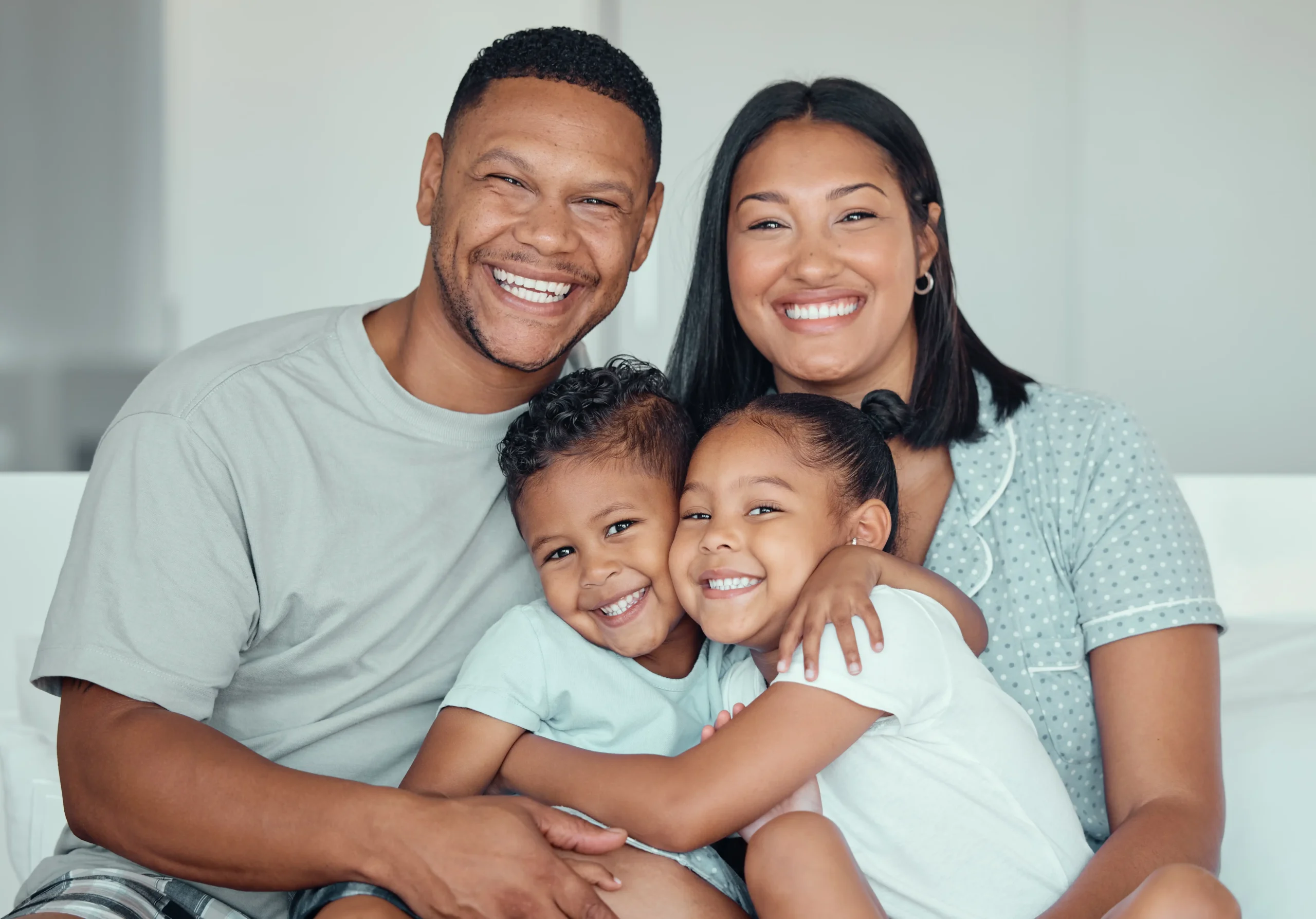 Smiling parents hugging their two children while sitting on a couch.