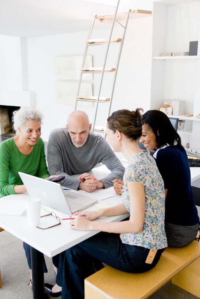 Diverse team discussing a project while gathered around a laptop in a bright office.